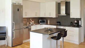 Una cocina moderna con armarios blancos, un refrigerador de acero inoxidable, un microondas y una cafetera.