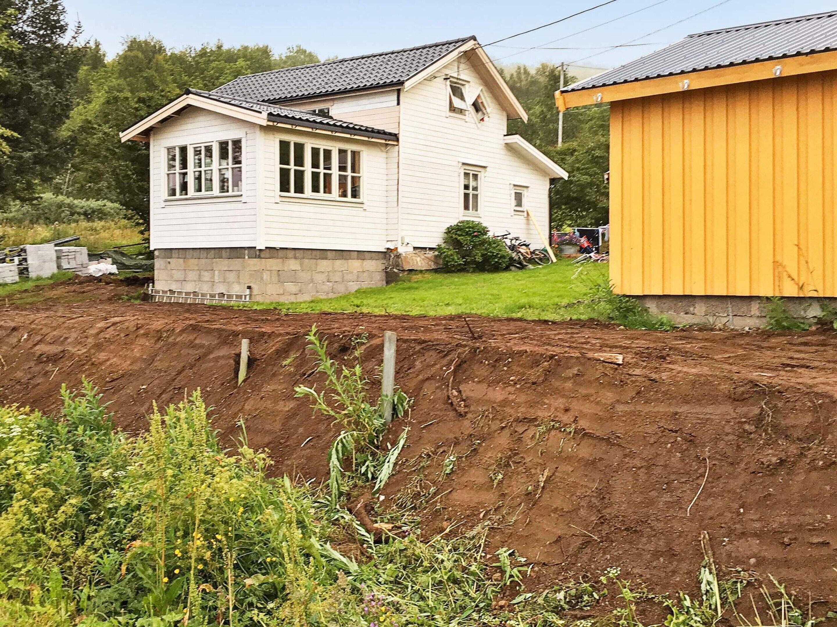 Una casa blanca con techo inclinado y un cobertizo amarillo en un entorno rural.