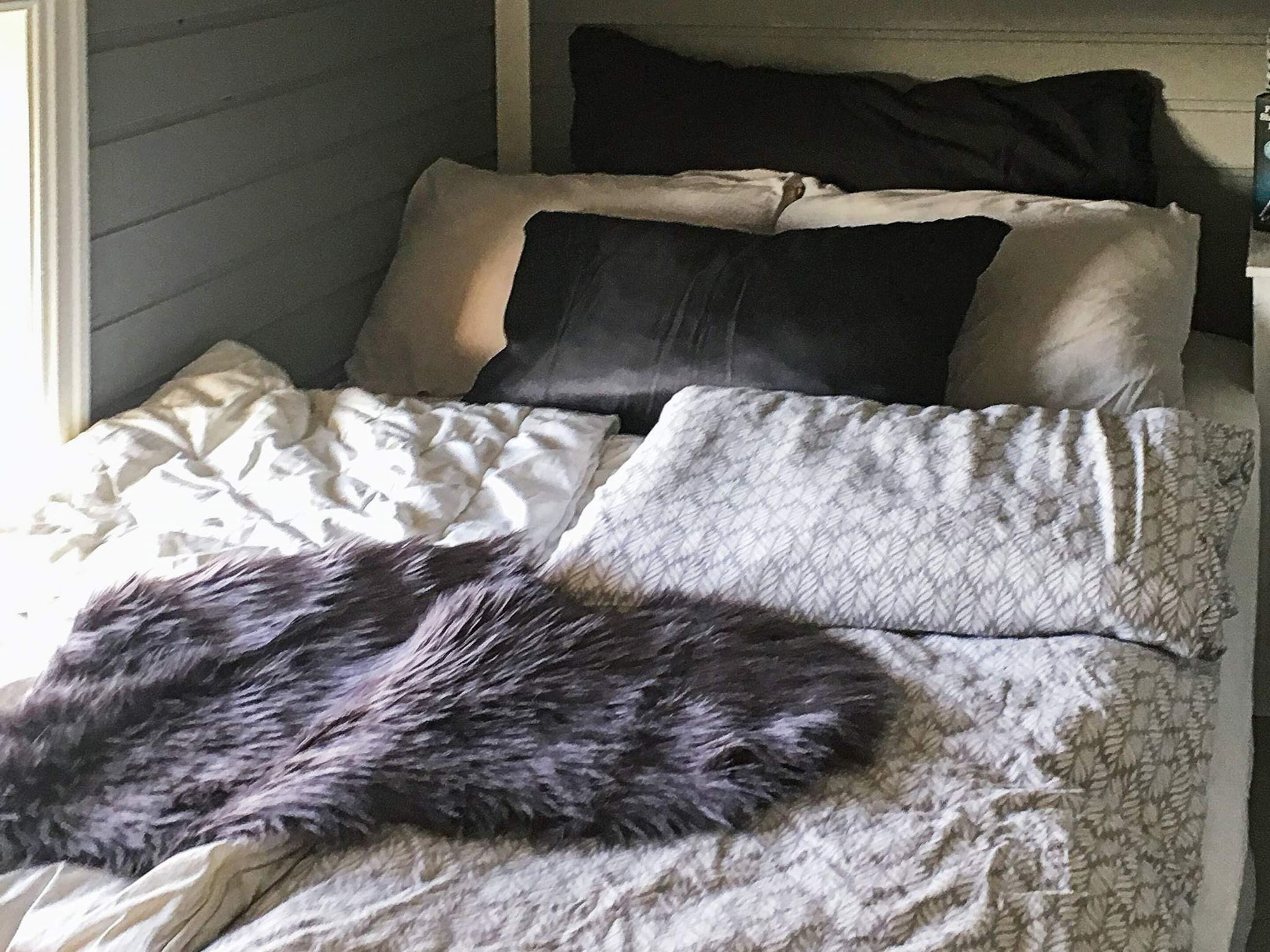 Een bed met een bontdeken, kussens en een bedovertrek met dessin.