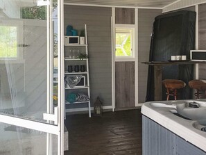 A compact room with a hot tub, a shelving unit with decorative items, and a window with a view.