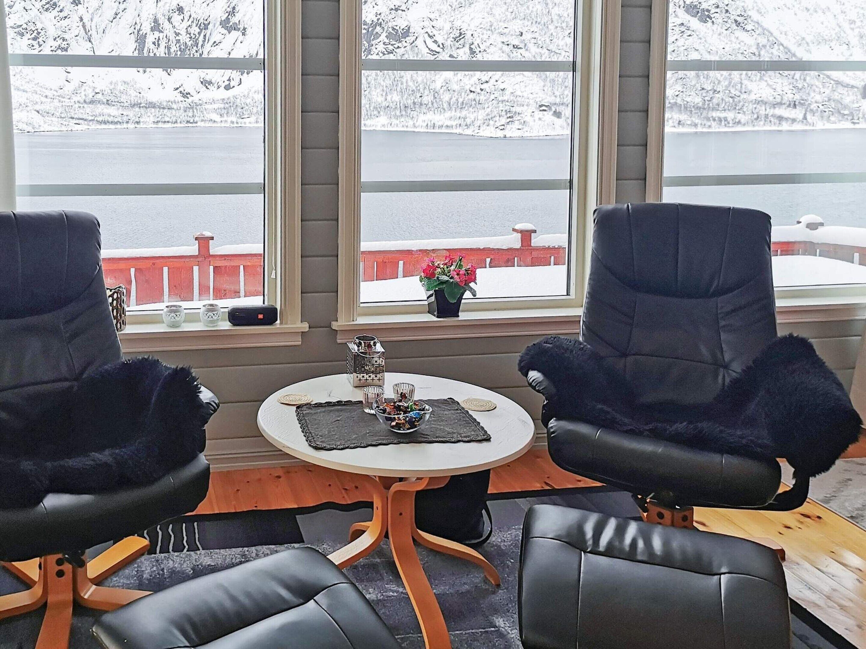 Una habitación con dos sillones de cuero negro, una mesita redonda con un posavasos y vistas a un paisaje nevado a través de amplias ventanas.