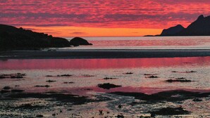 Una puesta de sol costera con afloramientos rocosos y aguas tranquilas que reflejan el cielo.