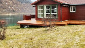 Una cabaña de madera con ventanas amplias, un balcón y vistas a un lago y montañas.