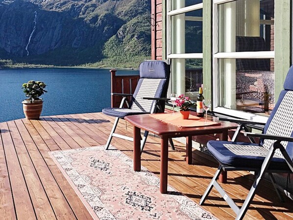 A wooden deck with a table and chairs, a potted plant, and a view of a lake and mountains. - Holiday Home in Tengelfjord (Hadsel)
