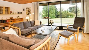 A modern living room with a wooden ceiling, large windows, a sofa, a coffee table, and a bookshelf. - 4 Person Holiday Home in Vaeggerlose (Vaeggerlose)