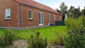 Un bâtiment en briques surmonté d’un toit de tuiles rouges, avec un petit jardin et une clôture en bois.