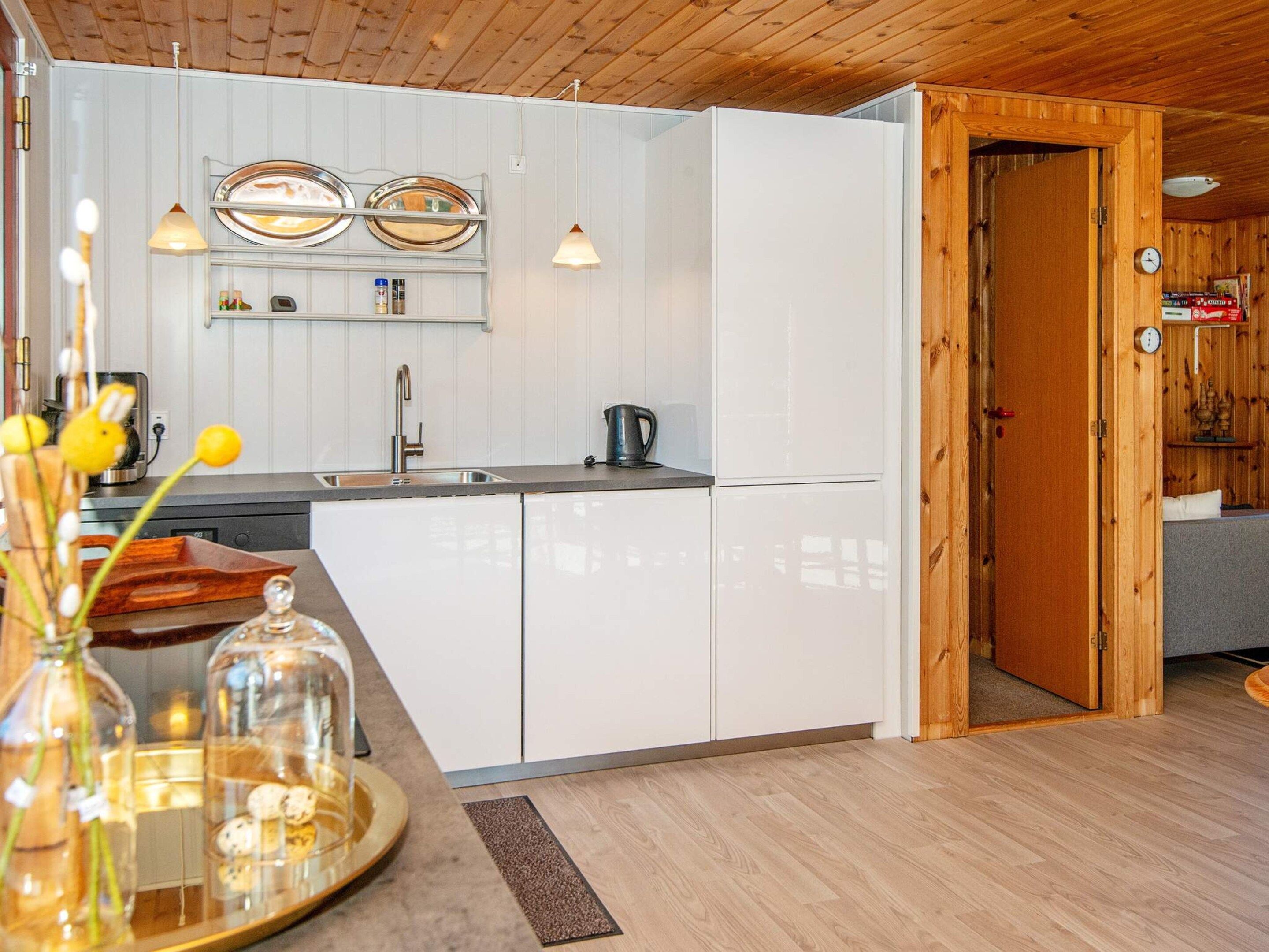 Una cocina moderna con armarios blancos, un fregadero y una cafetera. Se ve una puerta de madera que da a otra habitación.