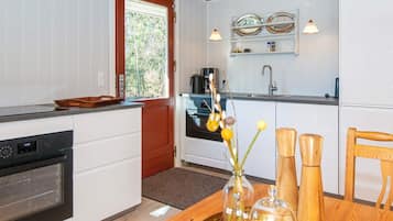 Una cocina moderna con armarios blancos, encimera de madera, horno empotrado, cafetera y ventana con vistas a árboles.