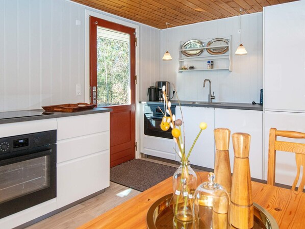 A modern kitchen with white cabinetry, a wooden countertop, a built-in oven, a coffee maker, and a window with a view of trees. - 4 Person Holiday Home in Ulfborg (Ulfborg)