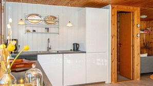 A modern kitchen with white cabinets, a sink, and a coffee maker. There is a wooden door leading to another room. - 4 Person Holiday Home in Ulfborg (Ulfborg)