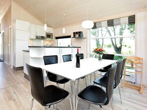 A modern kitchen with white cabinets, a dining table with black chairs, and a wine bottle on the table. - Holiday Home in Großenbrode (Grossenbrode)