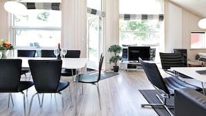 Ein moderner Essbereich mit hohen Decken und großen Fenstern, mit schwarzen Stühlen und einem weißen Tisch.