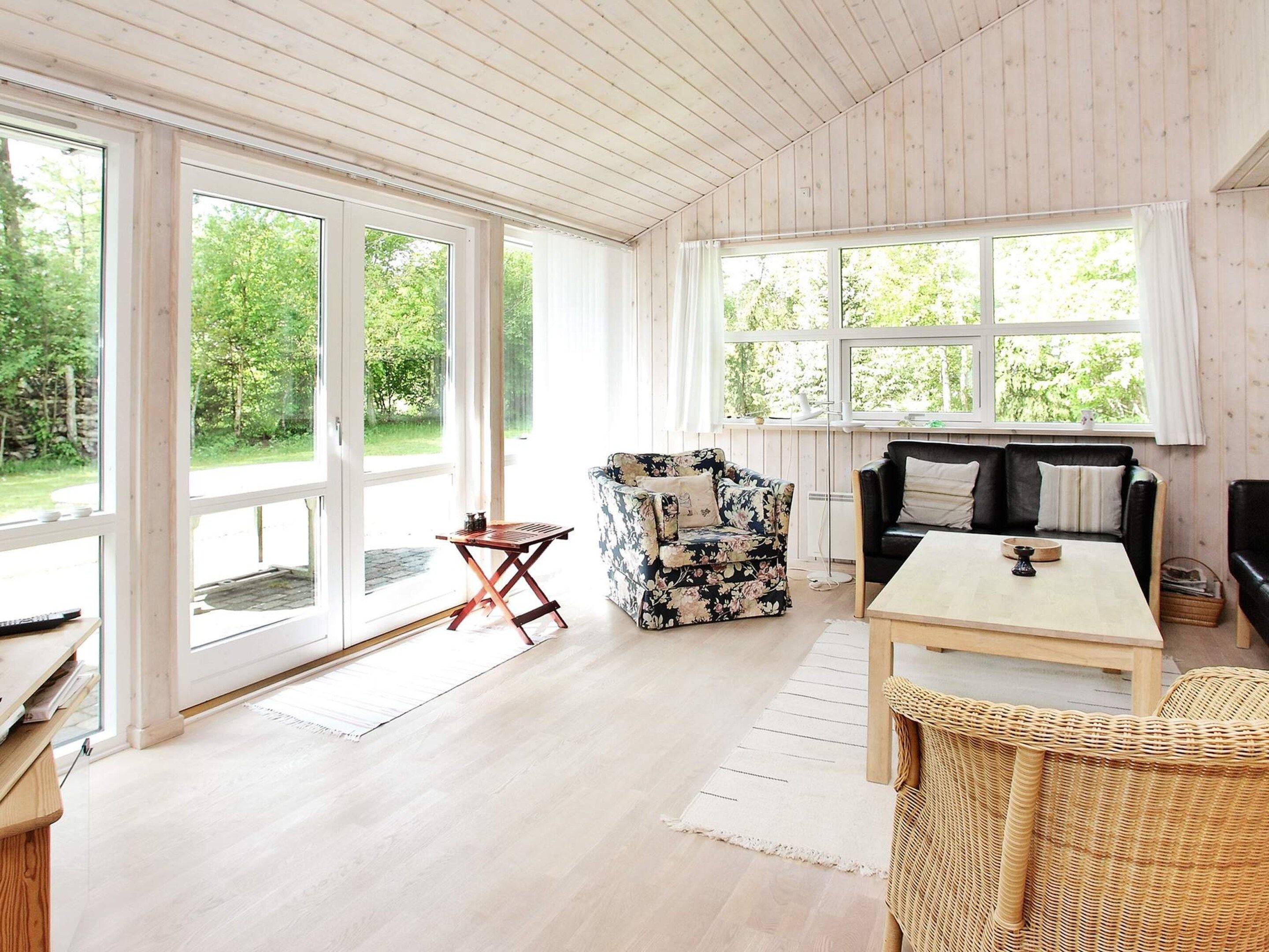 Una habitación con suelo de madera, un sofá, una mesa y una silla. Cuenta con ventanas amplias y una puerta que da al exterior.