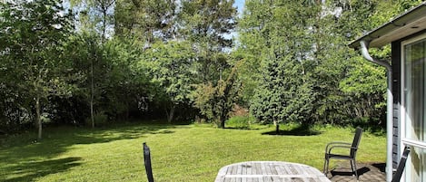 A patio area with a round wooden table and two chairs, surrounded by a grassy lawn and trees.