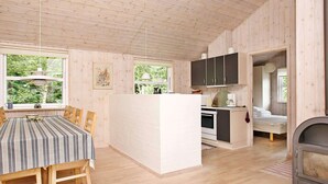 A cozy cabin interior with a dining area, kitchen, and a fireplace. - 4 Star Holiday Home in Albaek (Aalbaek)