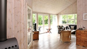 A spacious room with wooden walls and floors, a large window, a fireplace, a television, and a dining area with chairs and a table. - 4 Star Holiday Home in Albaek (Aalbaek)