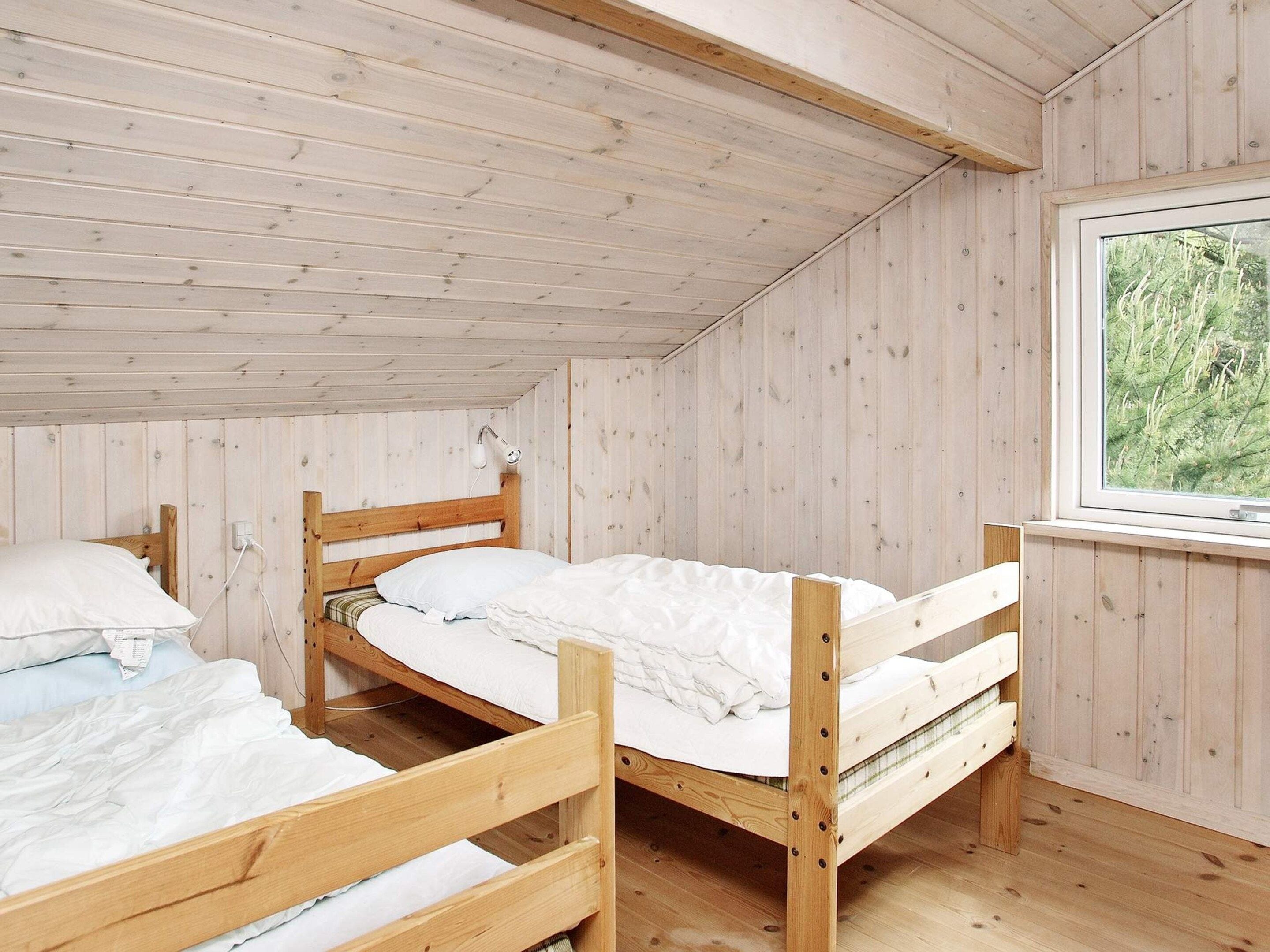 A cabin with two wooden bunk beds, a window with a view of greenery, and a wooden ceiling.