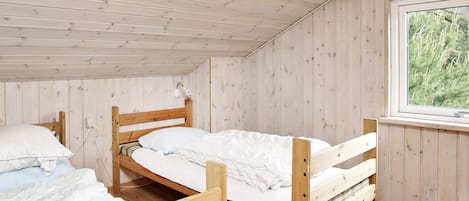 A cabin with two wooden bunk beds, a window with a view of greenery, and a wooden ceiling.