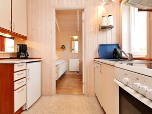 Cocina compacta con paredes de madera, una cama al fondo y un ventanal que proporciona luz natural.