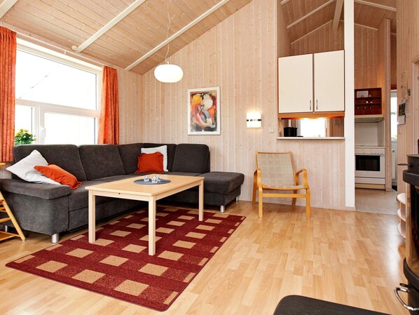 Una sala acogedora con un sofá, una mesita, una silla y una zona de cocina con armarios y una estufa.