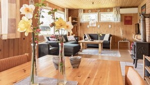 A cozy cabin interior with wooden walls, a dining table, sofas, and a fireplace. - Secluded Holiday Home in Jutland near Beach (Hals)