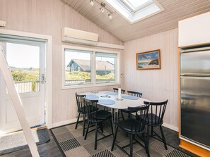 A dining area with a round table, black chairs, a painting on the wall, and a view of houses through the windows.