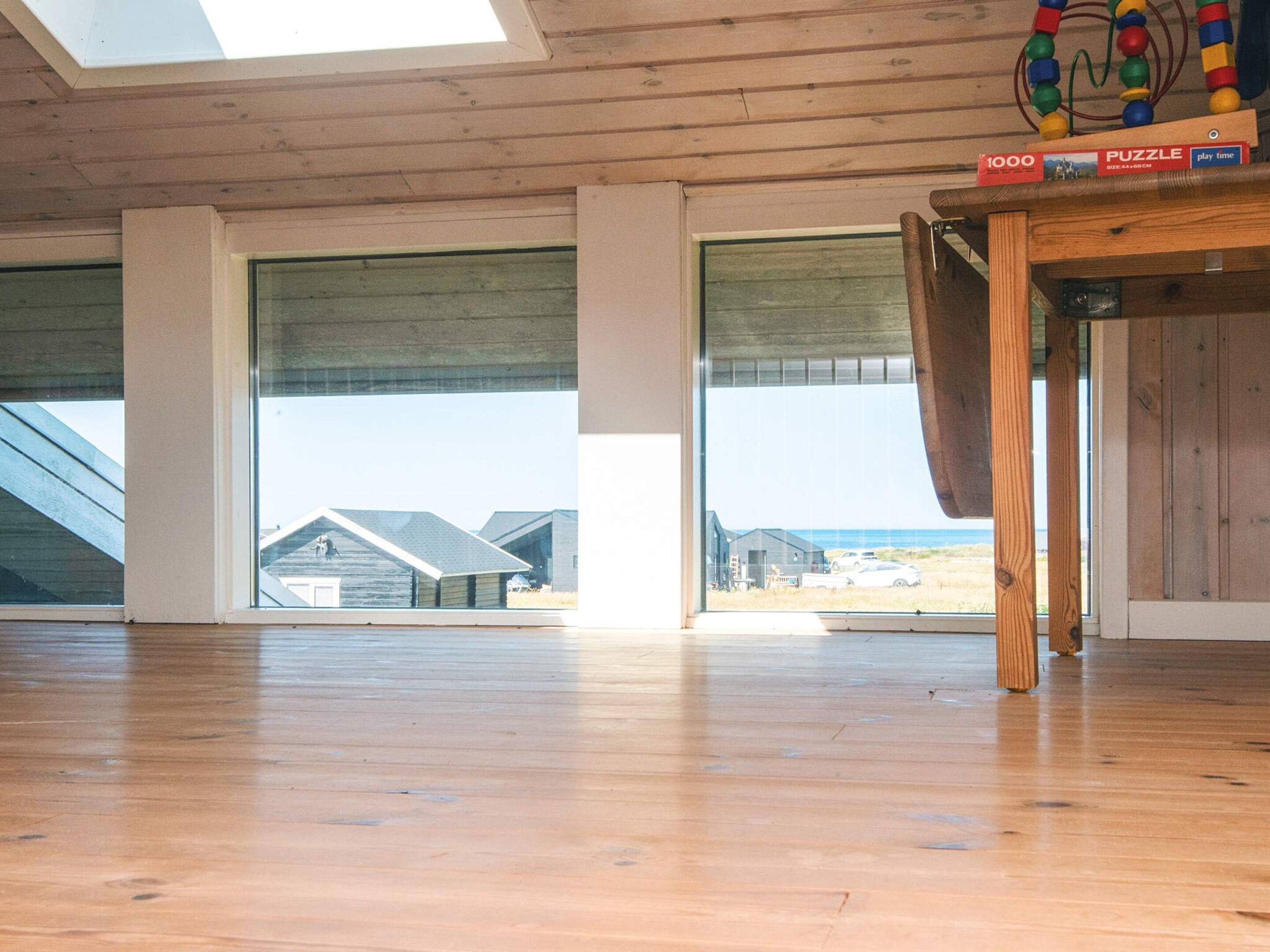 Una habitación amplia con ventanas grandes, piso de madera y un rompecabezas sobre una mesa.