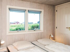 A room with two beds, a window with blinds, a door, and a bedside lamp.
