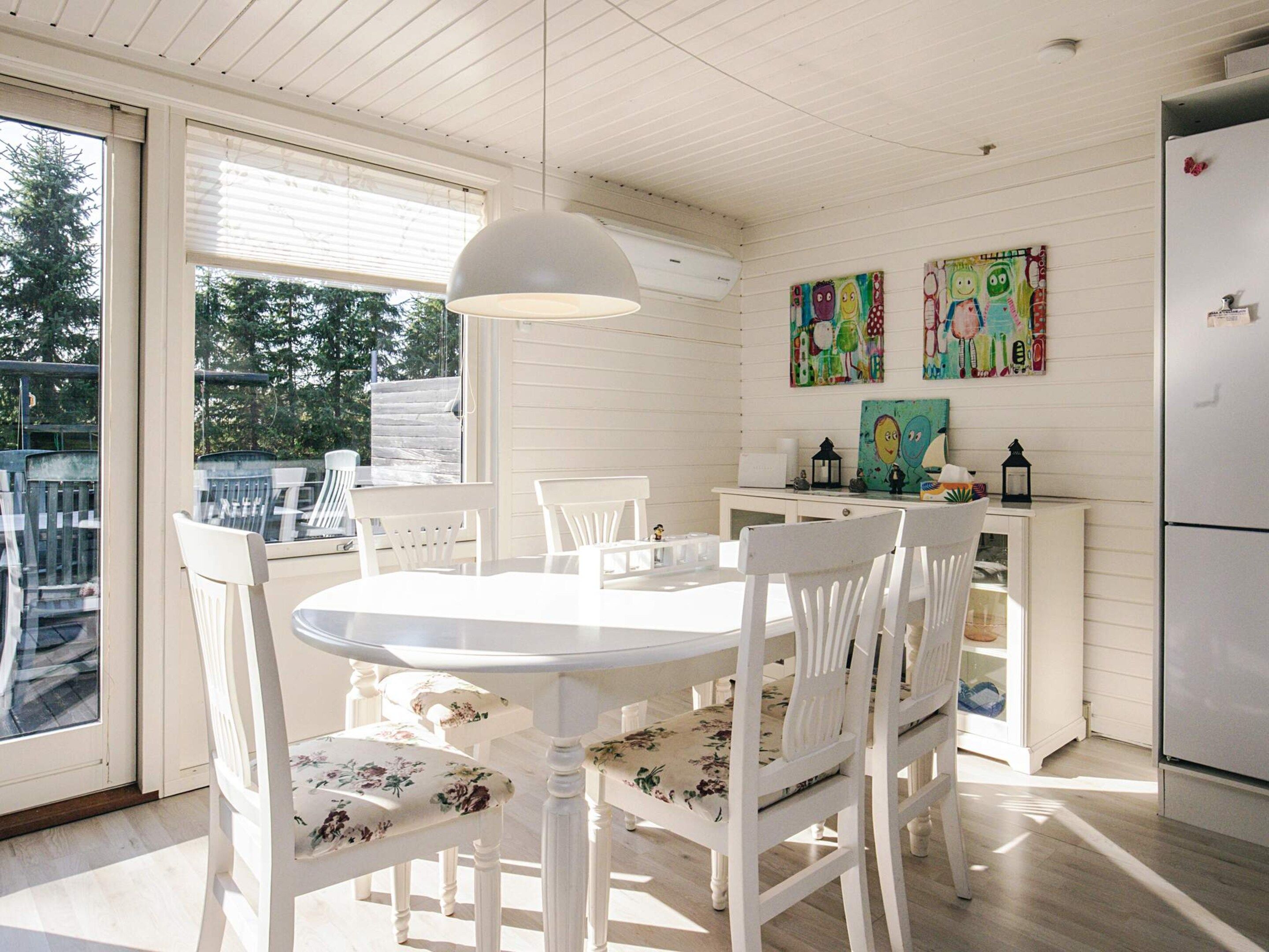 Un comedor con una mesa y sillas blancas, una lámpara colgante y una obra de arte en la pared.