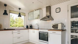 Una cocina moderna con armarios blancos, horno integrado, microondas y una ventana con persianas.