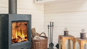 Una estufa de leña con fuego, una cesta de mimbre, un candelabro de metal y un mueble de madera con puertas de vidrio.