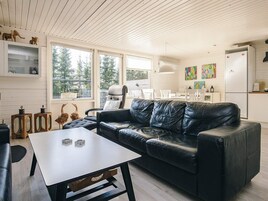 A modern living room with a black leather sofa, a white table, and a kitchen area with a refrigerator.