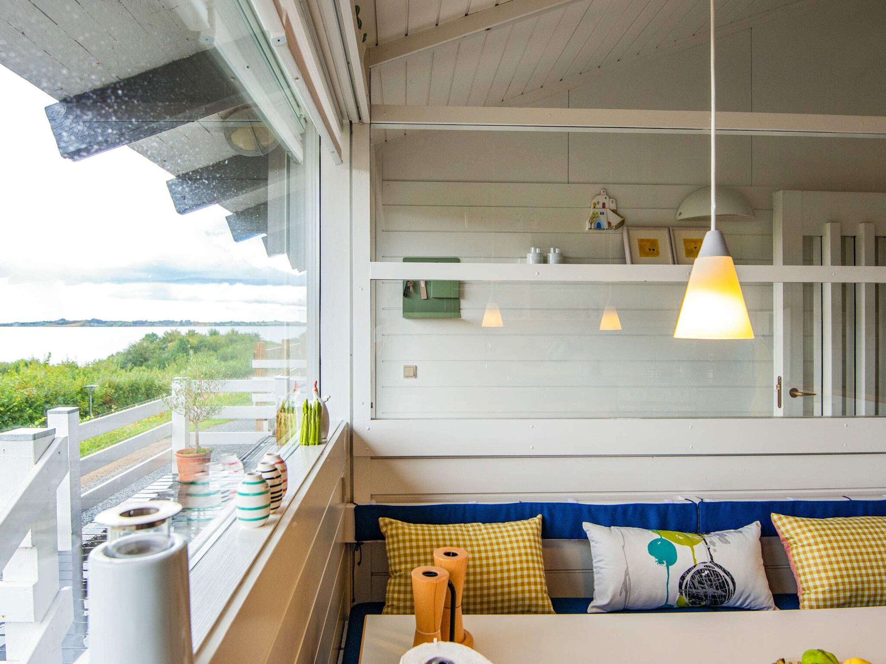 A room with a view of a lake, a balcony with outdoor seating, and pendant lighting.