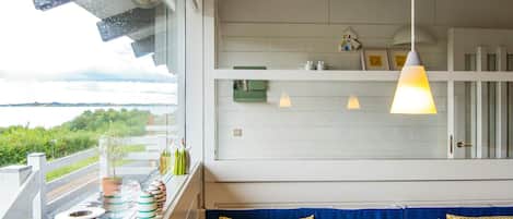 A room with a view of a lake, a balcony with outdoor seating, and pendant lighting.