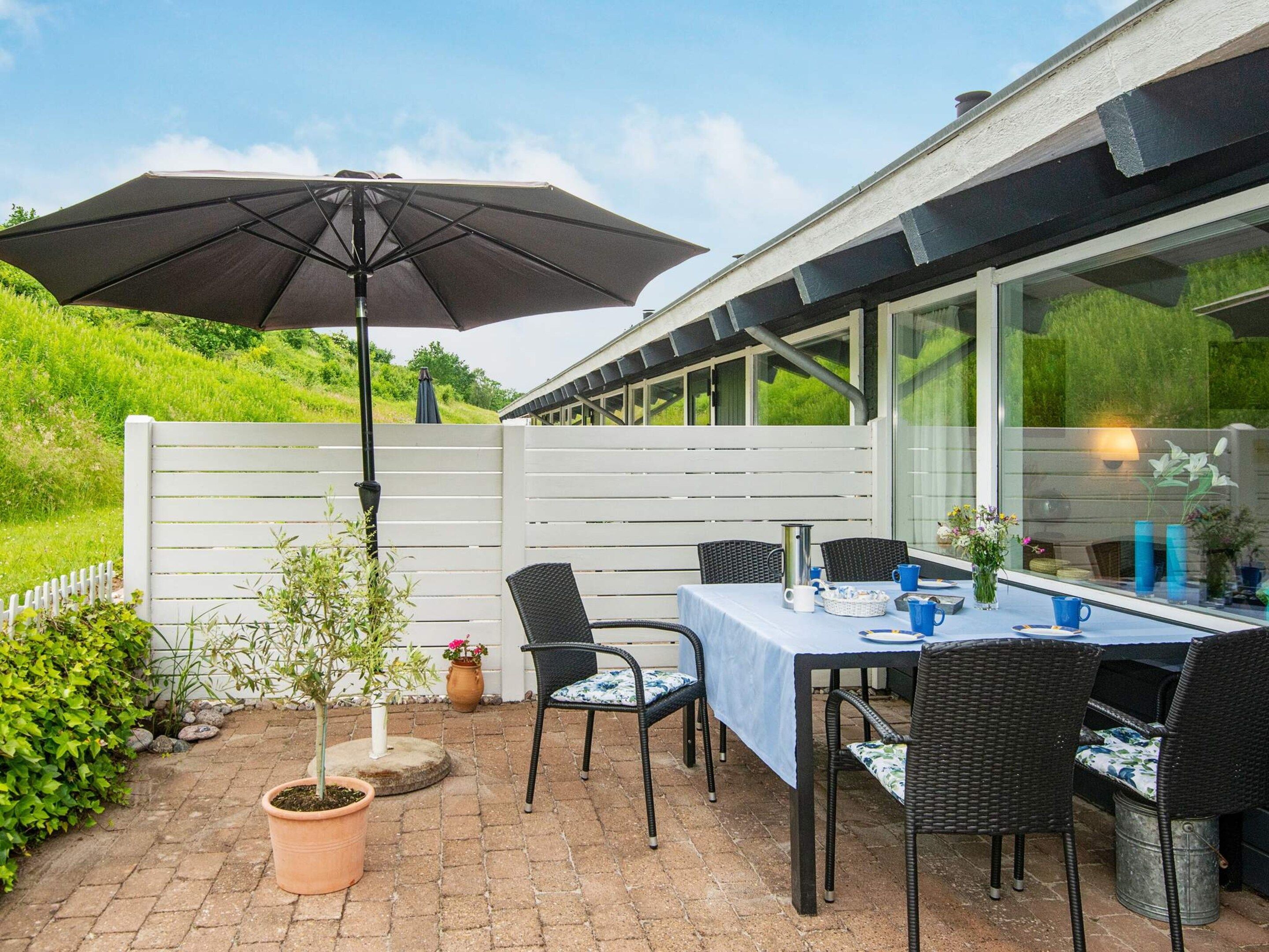 Una terrazza esterna con tavolo apparecchiato per consumare pasti, sedie, una pianta in vaso e un grande ombrellone.