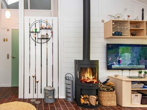 A living room with a wood-burning stove, a television mounted on the wall, and a decorative shelf with small items.