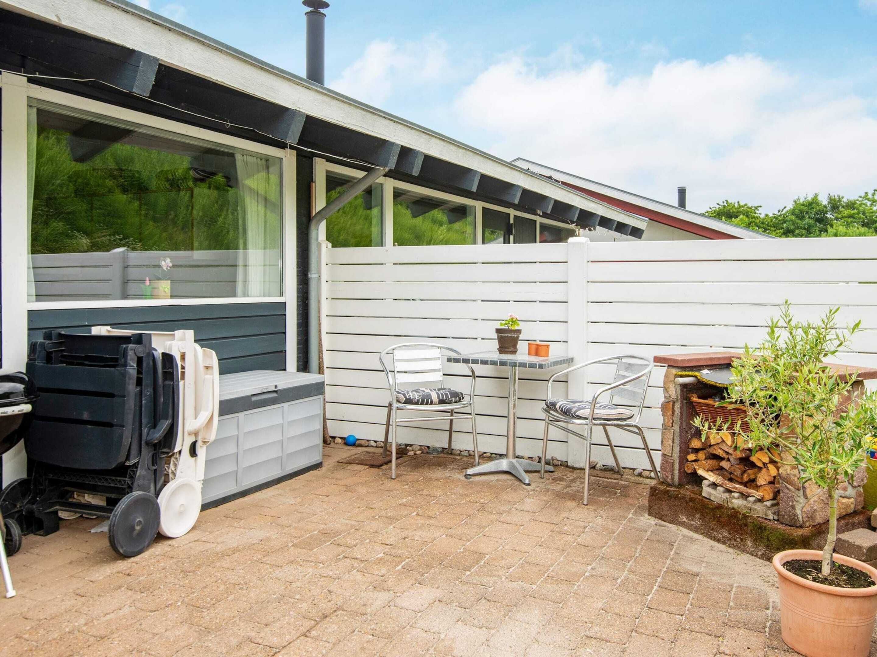 A patio with a table and chairs, a small garden area with a potted plant, and a white fence.