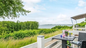 Um terraço com mesa e cadeiras, com vista para a água e vegetação.