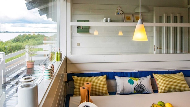 Quarto moderno com uma janela grande, sofá com almofadas estampadas e vista para o exterior.