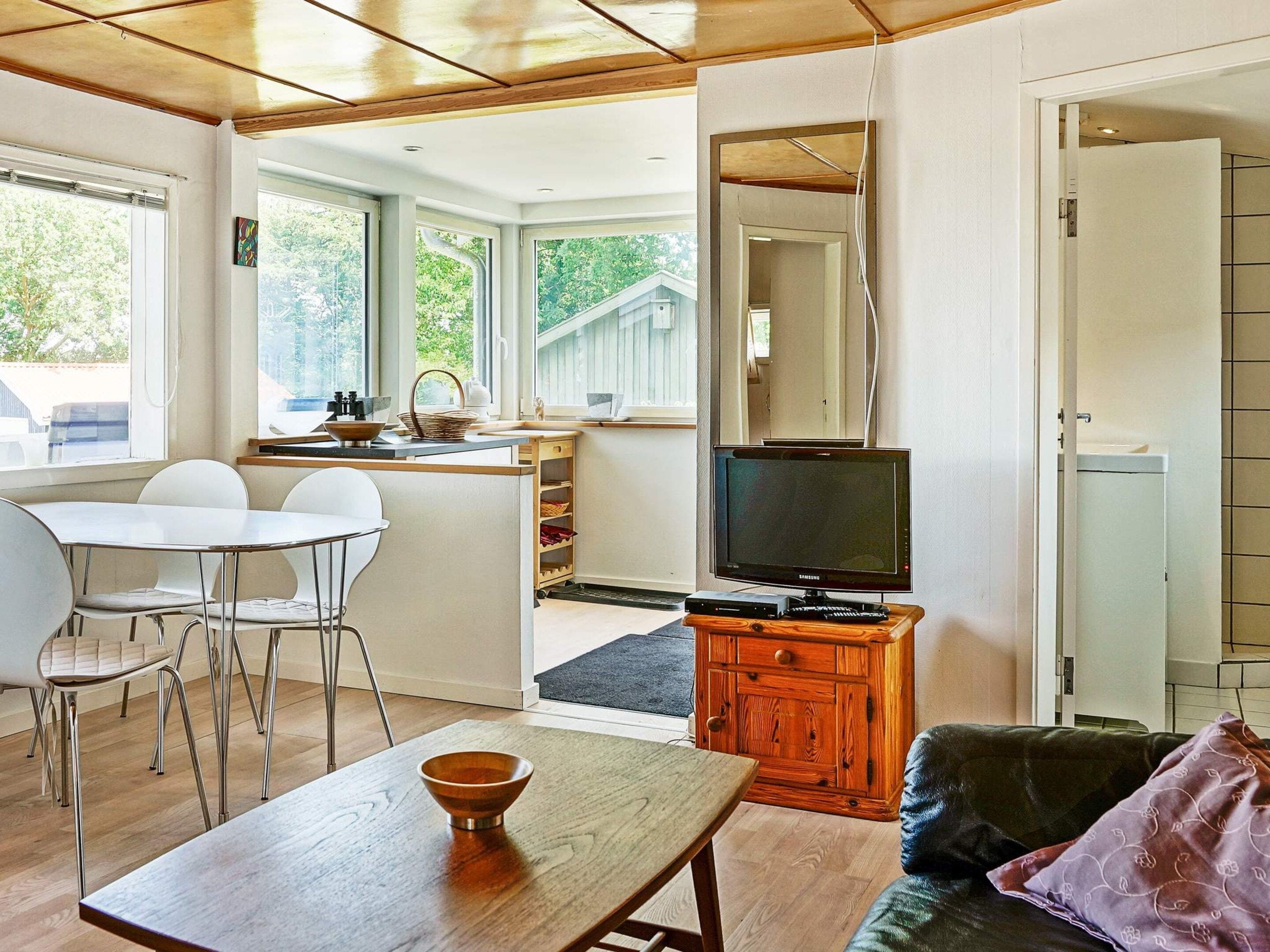 Una sala de estar moderna con una mesa de comedor de madera, un sofá y un televisor sobre un mueble de madera.