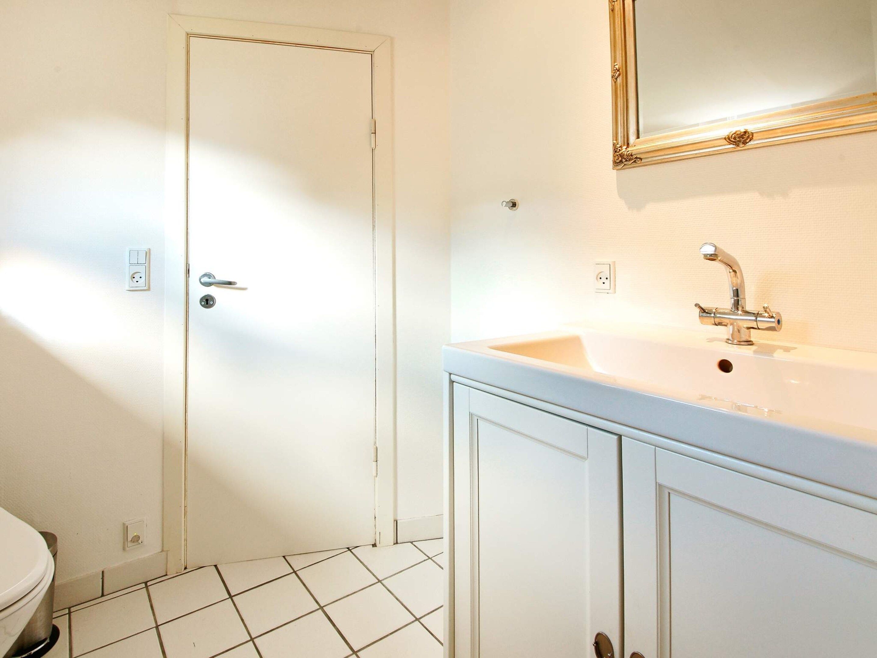 A bathroom with a white door, a sink with a mirror above it, and a toilet.