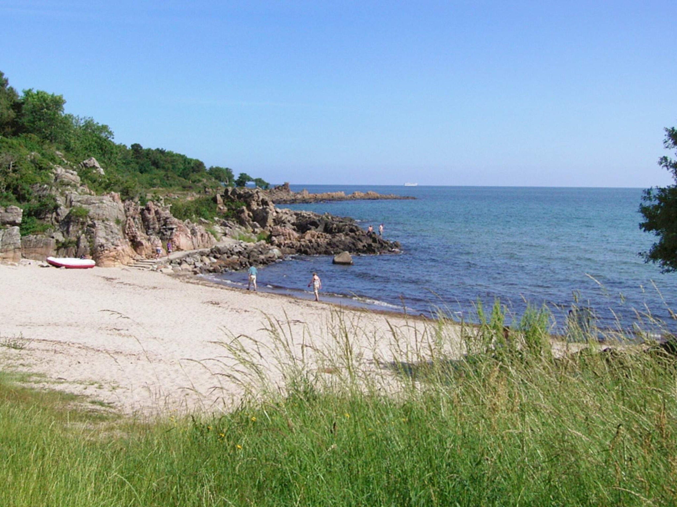A beach with rocky cliffs, a clear sky, and calm sea.