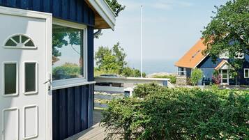 Una casa costera con una terraza de madera, una puerta blanca y vista al mar.