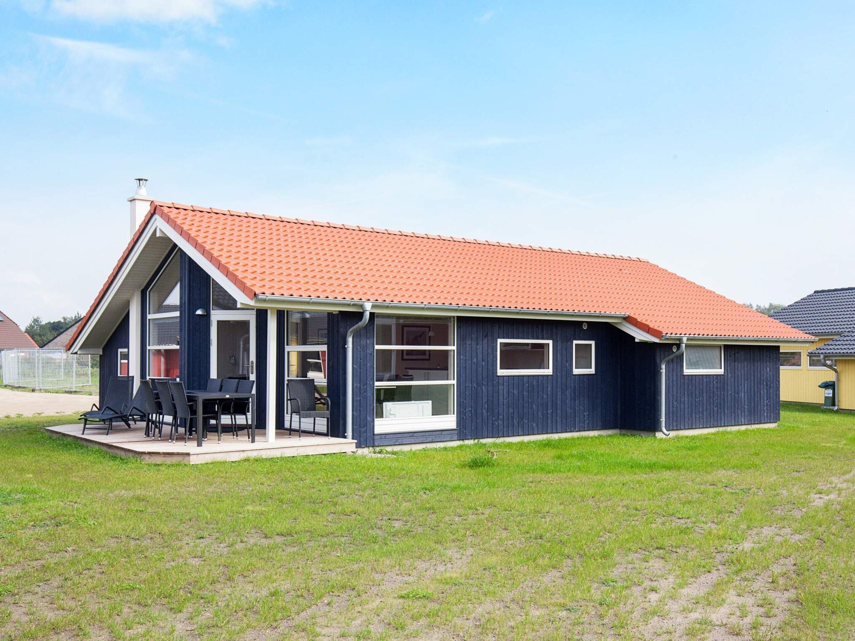 A single-story house with a red-tiled roof, large windows, and a patio area with outdoor seating.