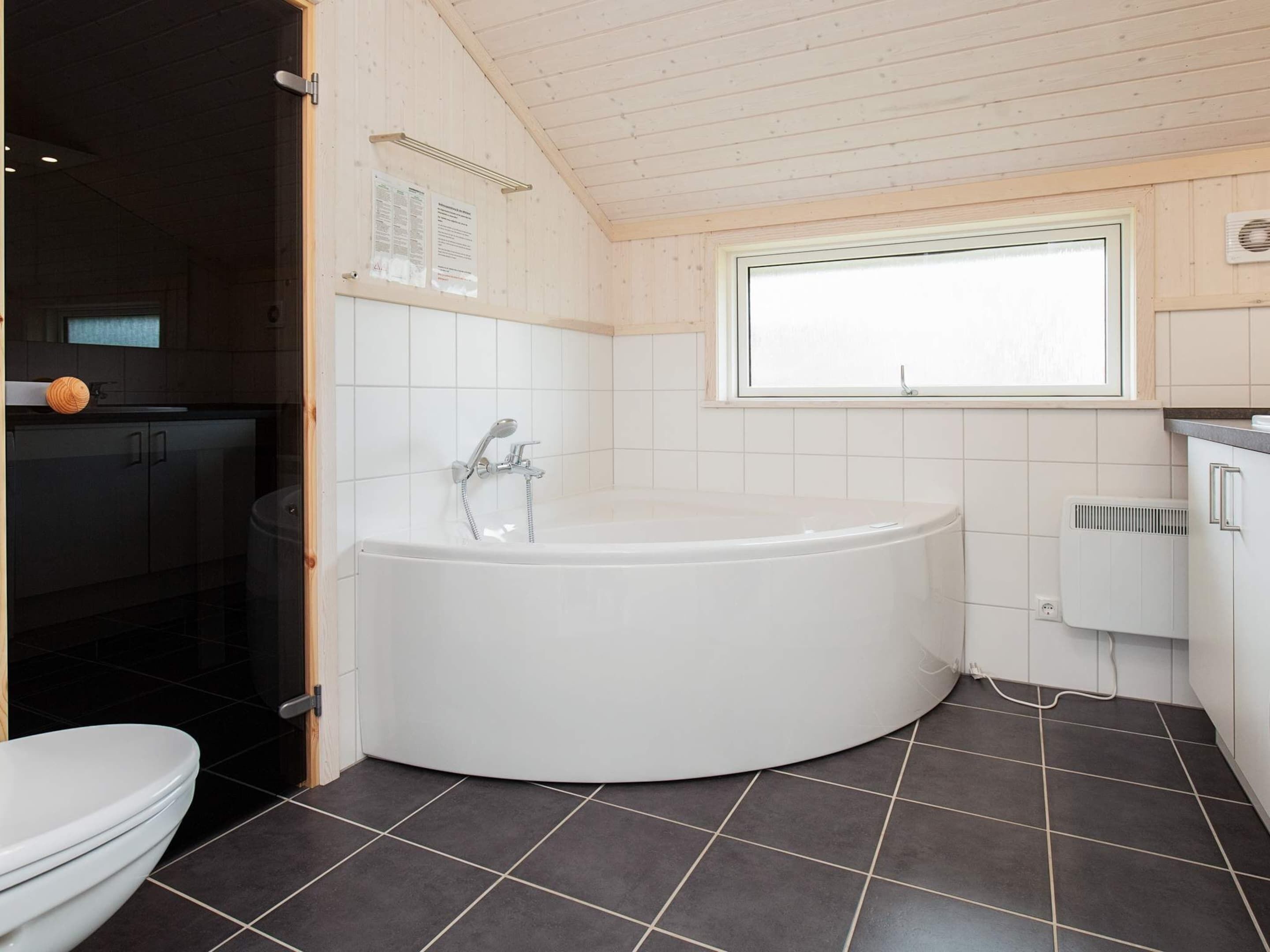 Un bagno moderno con una vasca da bagno indipendente, un water e una finestra che permette l'ingresso di luce naturale.