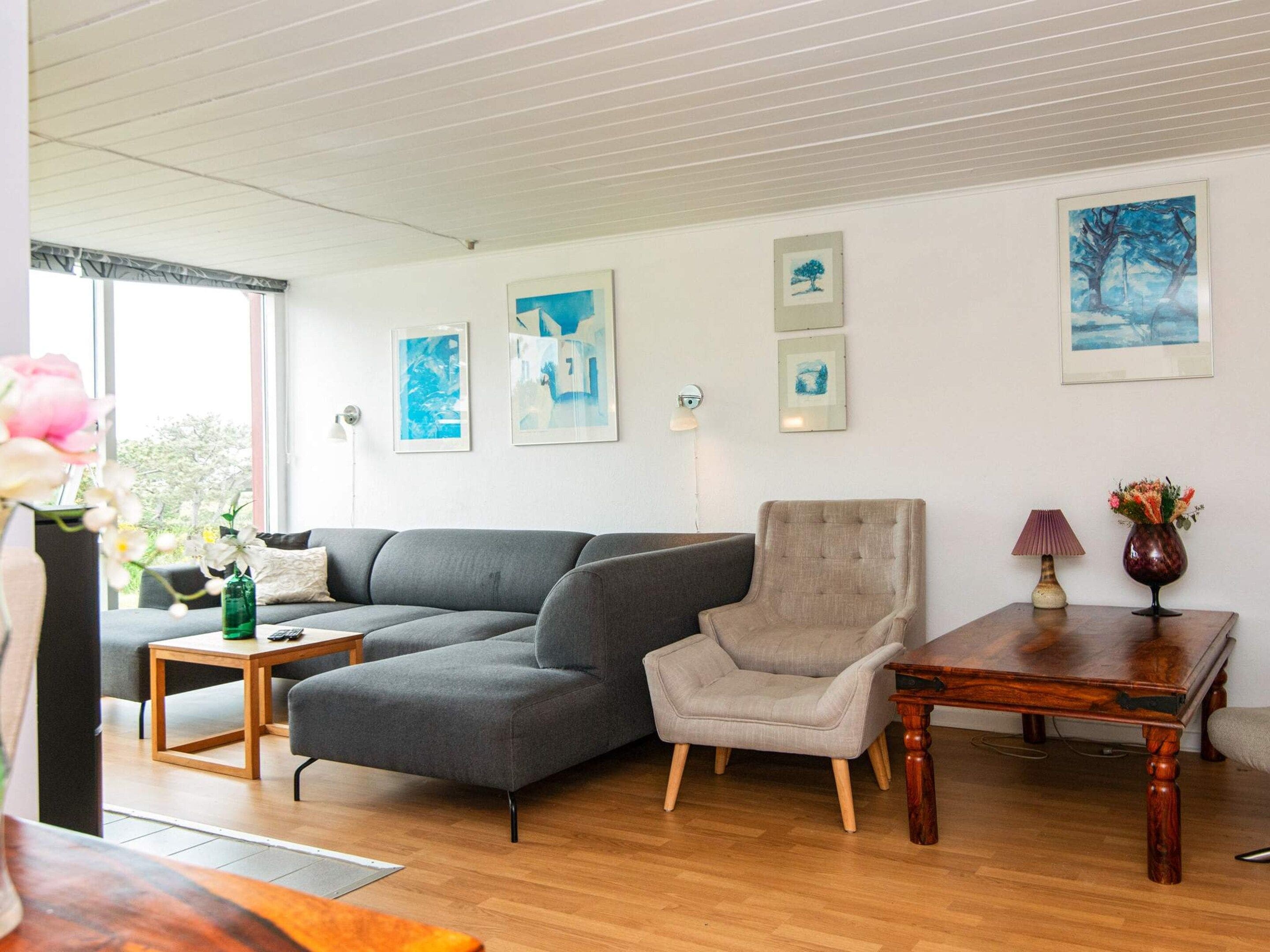 Un salon moderne avec un canapé gris, un fauteuil beige, une table basse en bois et une table d’appoint sur laquelle se trouvent une lampe et un vase.