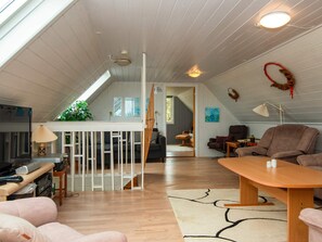 Ein großzügiger Wohnbereich mit hohen Decken, einem Esstisch, einer Couch und Blick ins Freie durch ein Fenster.