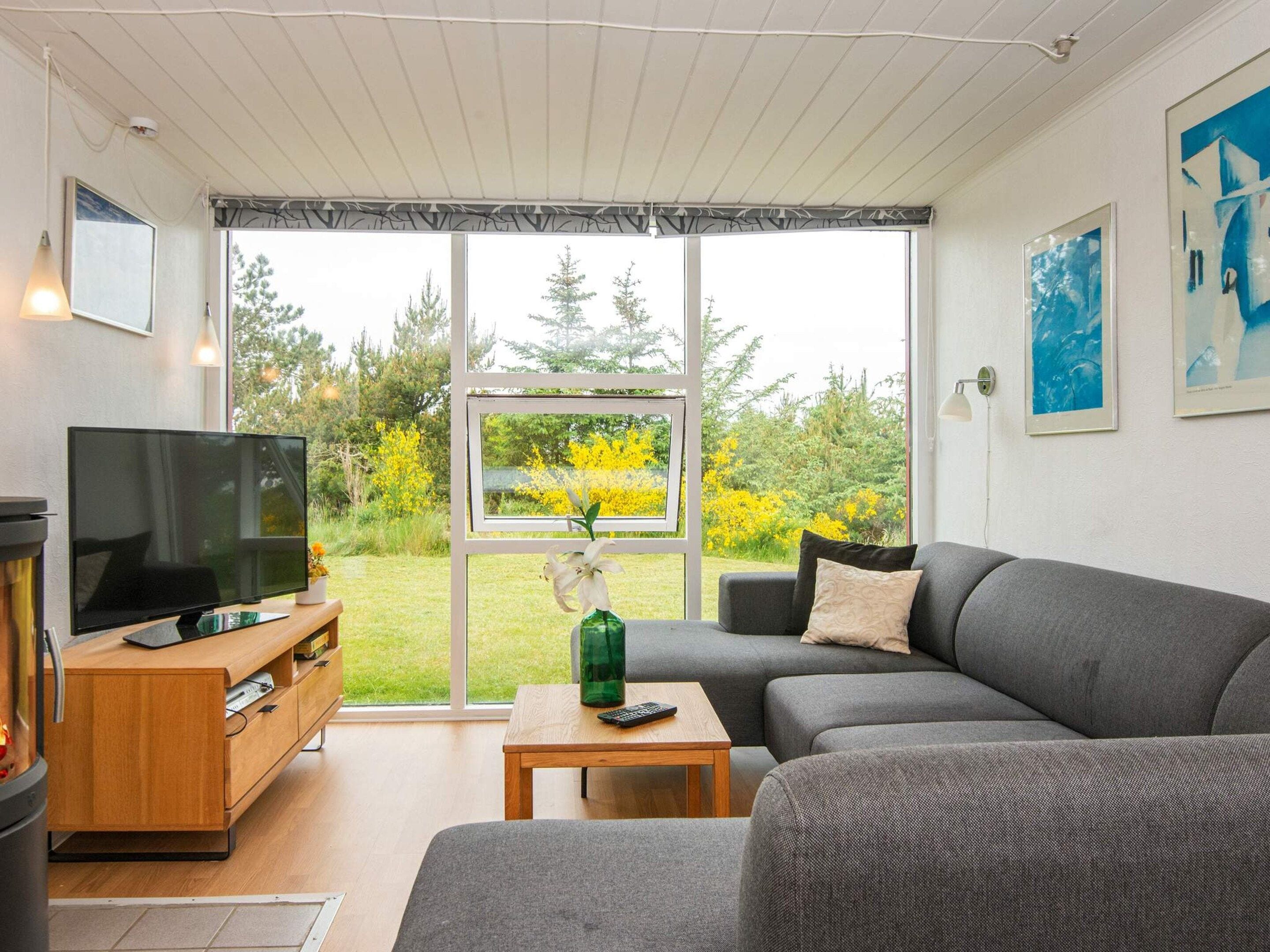 A modern living room with a television, sofa, and a view of a garden through large windows.