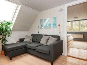 A modern loft bedroom with a grey sectional sofa, a potted plant, and a view of the outdoors through large windows. - Idyllic Holiday Home in Ulfborg with Hot Tub & Sauna (Ulfborg)
