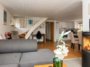 A modern living room with a gray sofa, a wooden coffee table, and a vase with white flowers. A staircase leads to an upper level with a kitchen area visible. - Idyllic Holiday Home in Ulfborg with Hot Tub & Sauna (Ulfborg)
